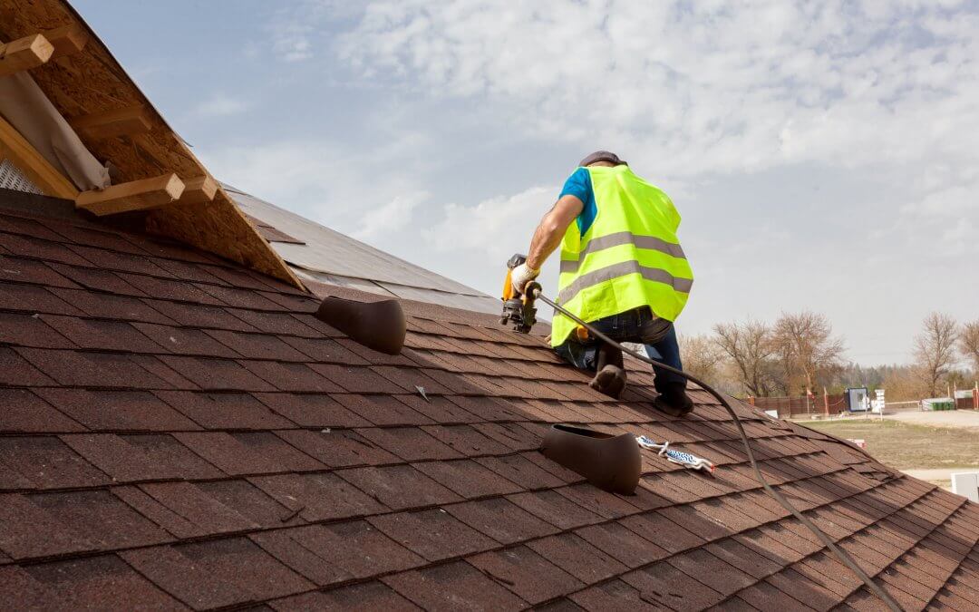 Construction worker putting the asphalt roofing (shingles) with nail gun on a large commercial apartment building development