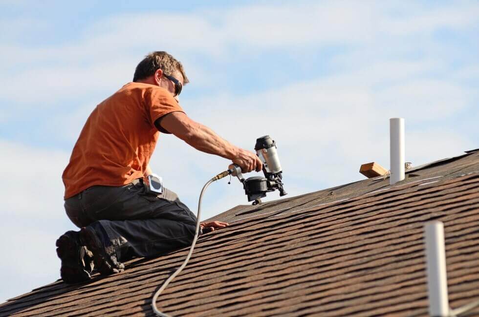 man securing new shingles on the roof of a home