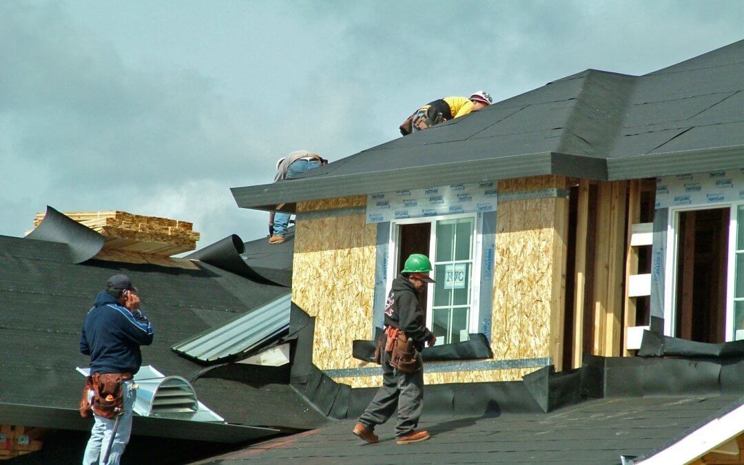 Roofers putting on felt paper over roof base before placing shingles